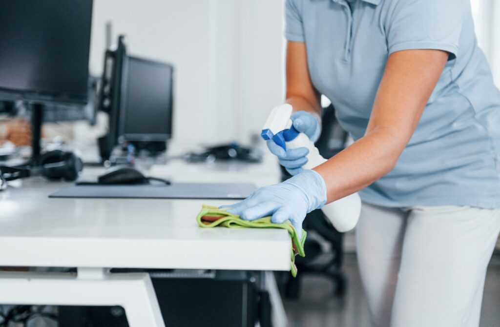 Close up view of woman in protective gloves that cleaning tables in the office